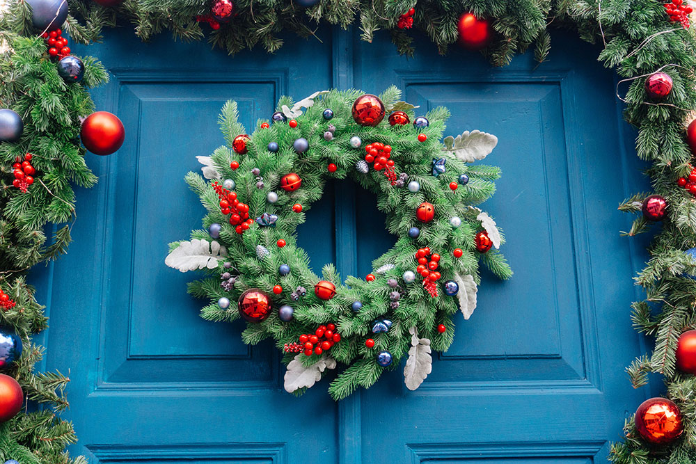 A fir wreath and garland decorated with ornaments and hung over a blue door